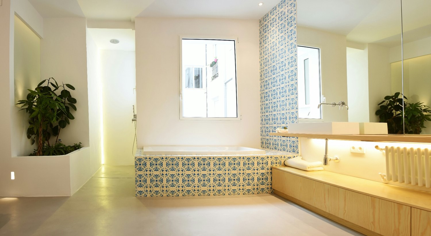 De izquierda a derecha: plantas en maceta integrada, ducha suspendida del techo con revestimiento de microcemento, bañera con paredes de baldosa hidráulica y mueble de baño de madera